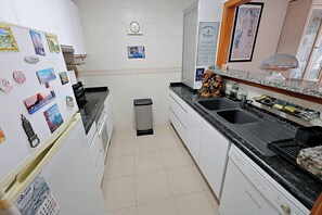 A kitchen with white cabinets, a black countertop, a sink, and a trash bin. - Sabine - apartment located in the heart of Calpe (Calpe)