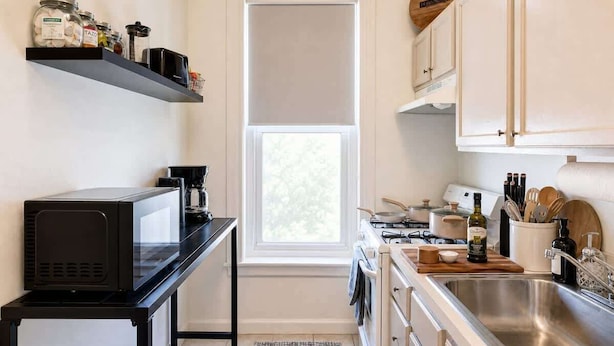 Una cocina compacta con microondas, estufa, pileta y estantes con frascos.