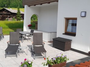 An outdoor patio with wicker furniture, a table, and potted plants. - Adlerblick by Interhome (Auffach)