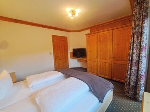 Un dormitorio con cama, televisión, armarios de madera y cortina estampada.