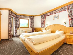 A double bed with a wooden headboard, a desk, and a chair in a room with floral curtains and a window. - Adlerblick by Interhome (Auffach)
