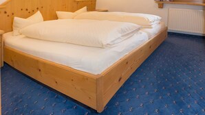 Una cama doble con cabecera de madera, ropa de cama blanca y una alfombra estampada en azul.