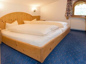 Ein Doppelbett mit Holz Kopfteil, weißer Bettwäsche und einem blau gemusterten Teppich.
