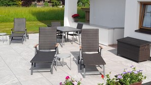 Un patio al aire libre con mobiliario de mimbre, una mesa y plantas en macetas.