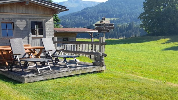 A wooden building with a deck, outdoor seating, and a signpost with destination names. - Schatzberg by Interhome (Auffach)