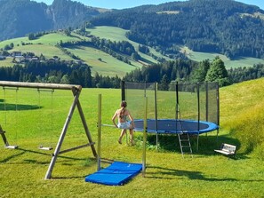 Ein Trampolin auf einer grünen Wiese, in der Nähe ein Schaukelstuhl.
