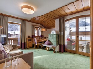 Ein gemütliches Zimmer mit Holzbalkendecke, einem Essbereich und großen Fenstern mit Blick auf Schnee.