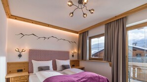 Ein Schlafzimmer mit einem hölzernen Kopfteil, einem großen Bett mit violetter Decke, zwei Nachttischen, einer Wandleuchte und einem Fenster mit Blick auf einen Berg.
