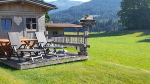 Ein hölzernes Gebäude mit einer Terrasse, Sitzgelegenheiten im Freien und einem Wegweiser mit Zielortnamen.