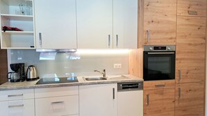A modern kitchen with white cabinets, a wooden accent wall, a built-in oven, and a coffee maker.