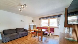 A living room with a sofa, a dining table with chairs, and a TV on a wooden stand.
