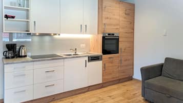 A modern kitchen with white cabinets, a wooden accent wall, a built-in oven, and a grey sofa in the living area.