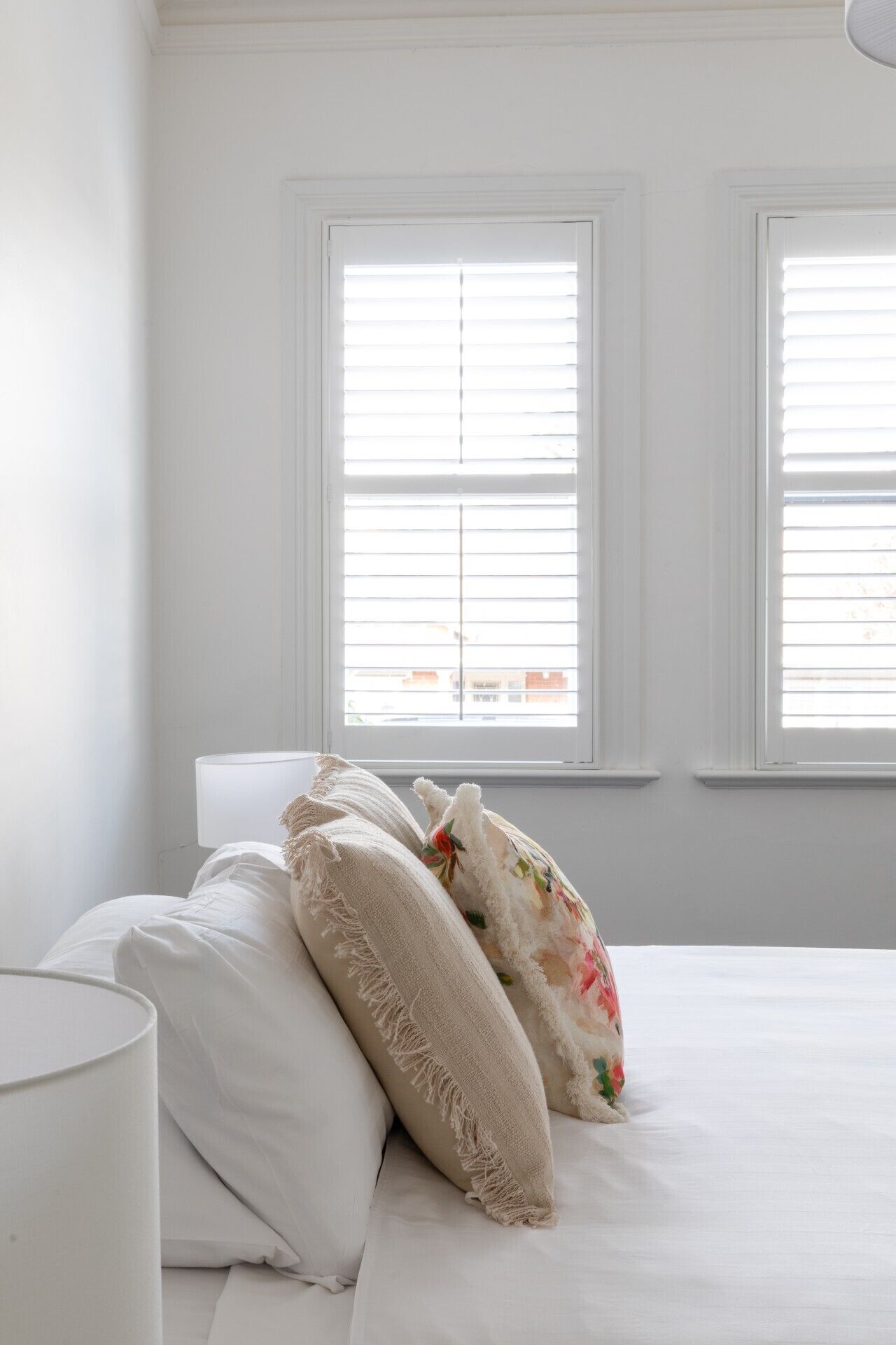 A bedroom with a bed, pillows, and two windows with blinds.