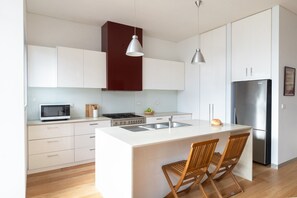 Eine moderne Küche mit weißen Schränken, einer zentralen Kochinsel mit Barhocker, einem Edelstahlkühlschrank und einer Mikrowelle.
