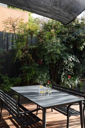 Eine Terrassengruppe mit Tisch und Bänken, umgeben von dichtem Grün und einem Holenzaun.