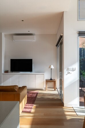 Een moderne woonkamer met een flatscreen televisie, een bank, een lamp en een houten vloer.