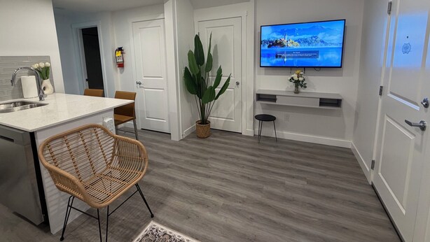 A modern kitchen with a dining area, a flat-screen TV mounted on the wall, and a potted plant. - Modern Rangeview Stay| Near YMCA & Cineplex Cinema (Calgary)