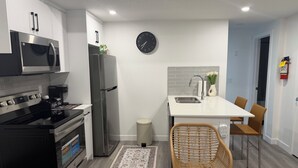 A modern kitchen with a microwave, stove, refrigerator, and a dining area with chairs and a table. - Modern Rangeview Stay| Near YMCA & Cineplex Cinema (Calgary)