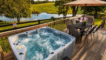 A hot tub on a wooden deck with a view of a lake and trees.