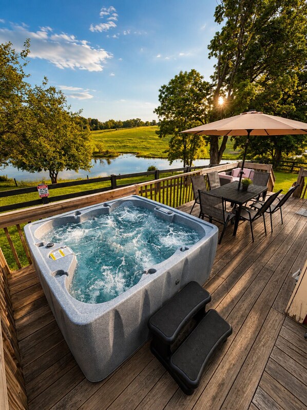 A hot tub on a wooden deck with a view of a lake and trees.