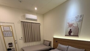 A hotel room with a bed, a bedside table, a wall-mounted air conditioner, a door with shoe storage, and a small trash bin. - Lying Flat Hostel (Minxiong)