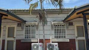 A building with two doors, each marked with a number, and a palm tree in the foreground. - Lying Flat Hostel (Minxiong)