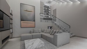 Una sala de estar moderna con un sofá seccional, una mesa de centro de mármol y una escalera con barandillas de vidrio.