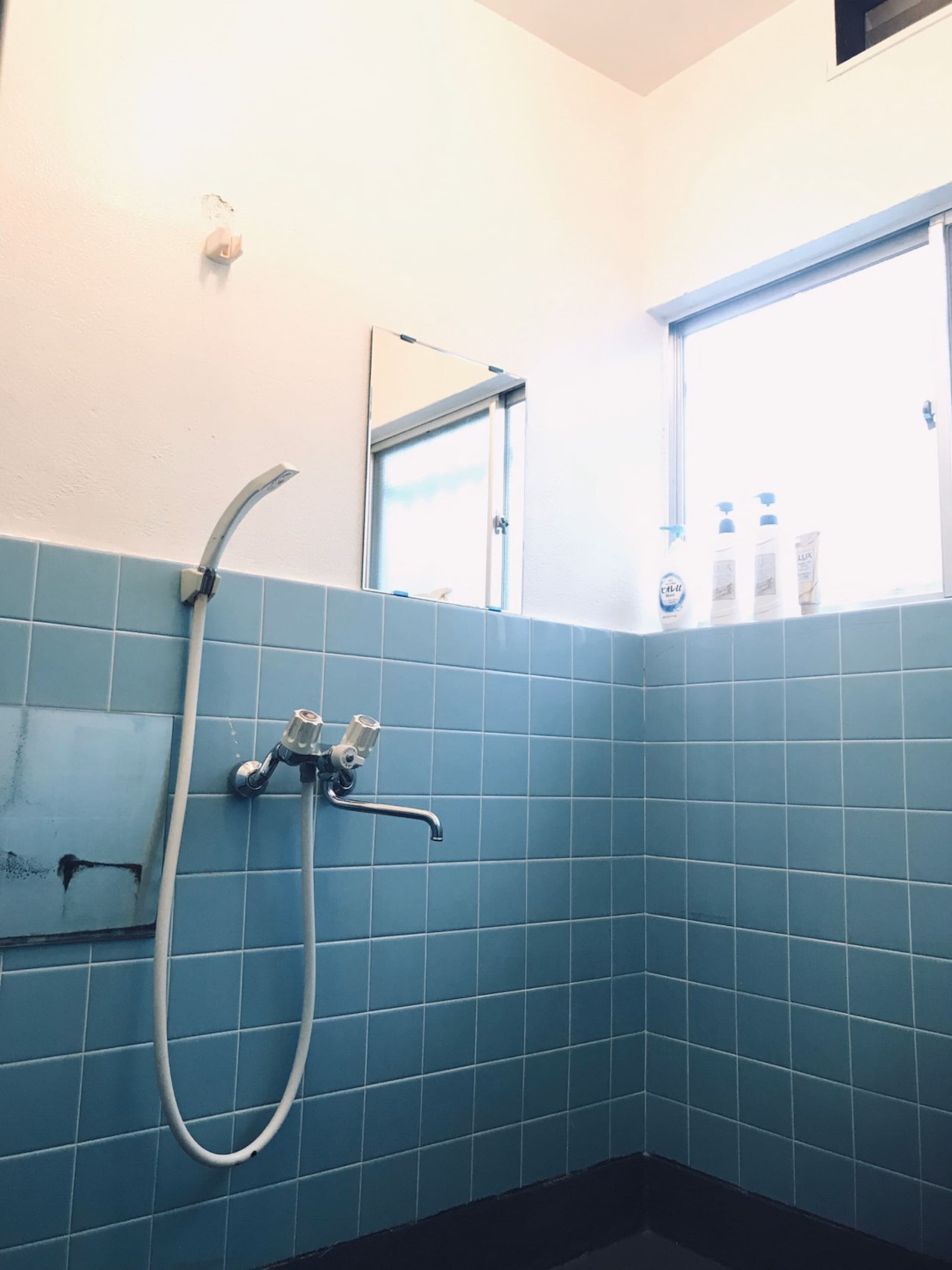 A bathroom with blue tiles, a shower, a window, and toiletries on the windowsill.