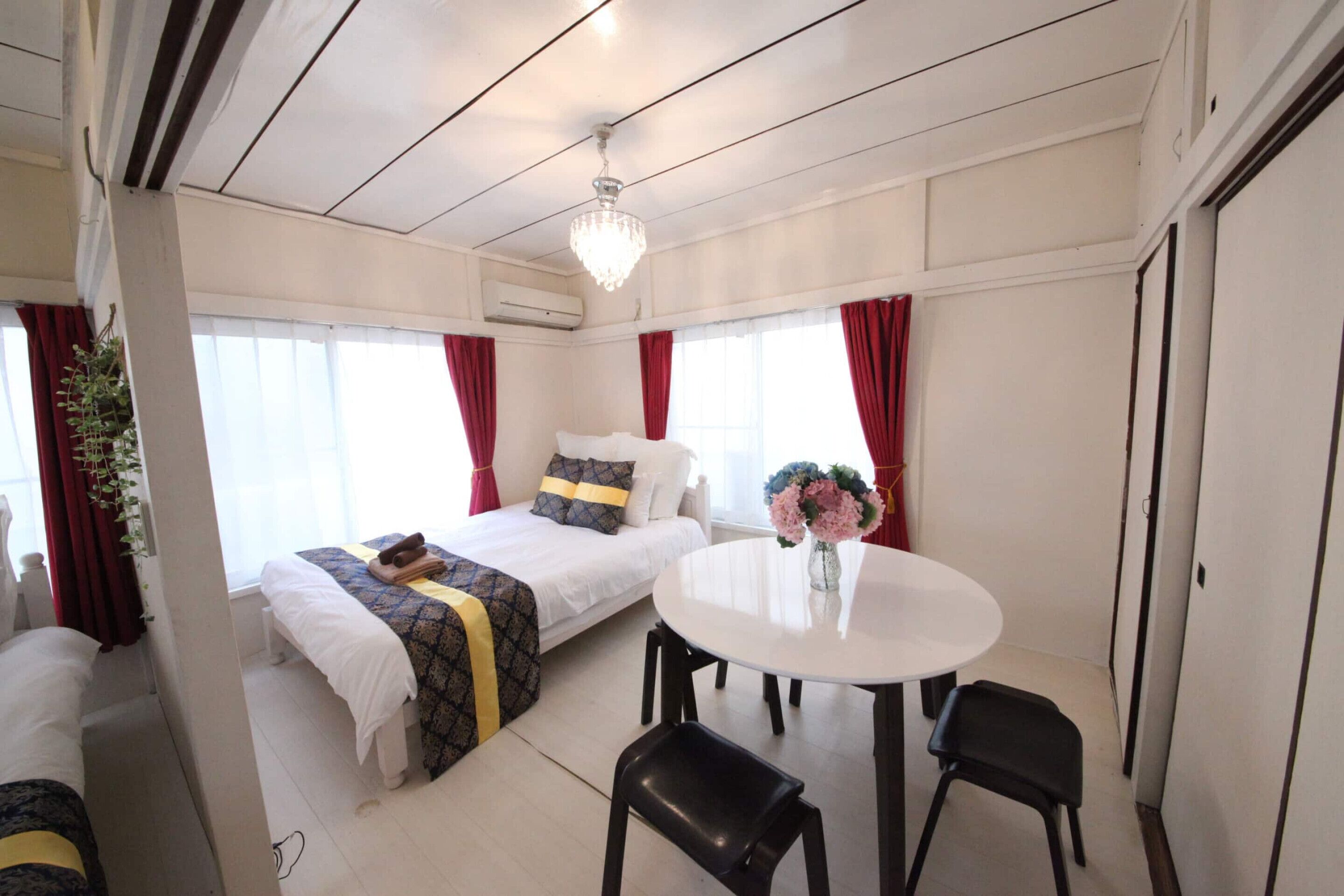 Ein Hotelzimmer mit einem Bett, einem runden Esstisch, zwei Stühlen, einer Deckenleuchte und einem Fenster mit Vorhängen.