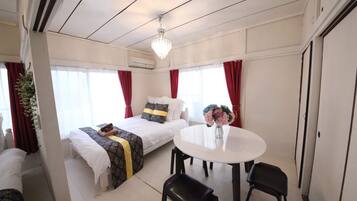 Ein Hotelzimmer mit einem Bett, einem runden Esstisch, zwei Stühlen, einer Deckenleuchte und einem Fenster mit Vorhängen.