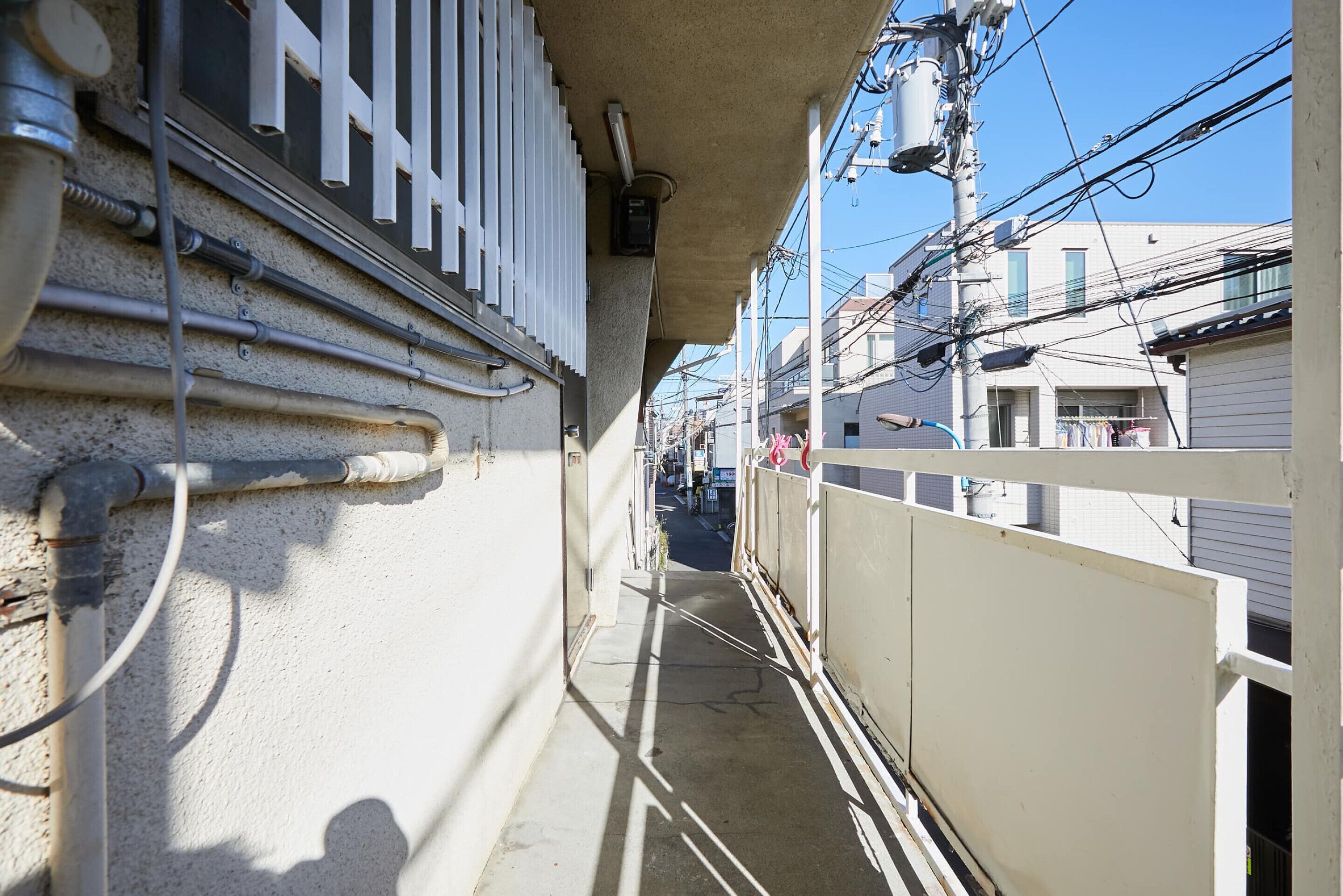 Un stretto vicolo con un recinto bianco, cavi elettrici aerei e edifici sullo sfondo.