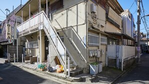 A multi-story building with a staircase leading to the entrance, a gated entrance, and a utility area with equipment. - RESIDENTIALHOTELDAIICHI-H OKUBO Room.2C (Tokyo)