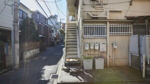 A narrow urban street with buildings on both sides, a drainage grate, and utility meters on the right. - RESIDENTIALHOTELDAIICHI-H OKUBO Room.2C (Tokyo)