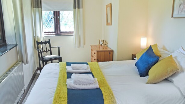 A neatly made bed with towels, a bedside table with a lamp, a chair, and a window with curtains. - Walnut Tree - UK52235 (Horning)