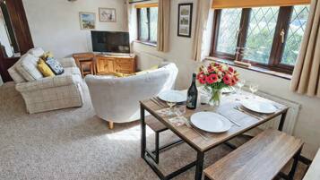 A dining area with a table set for two, a sofa, a television, and a window with curtains.