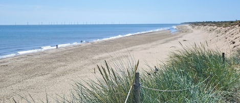 A beach with a clear sky, a sandy shore, and a fence in the foreground.