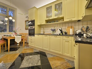 Een keuken met gele kastjes, een zwart-wit betegelde vloer en een eethoek met een tafel en stoelen.