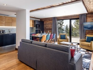 A modern living room with a sofa, a dining area with chairs, a kitchen, and a balcony with a view. - Résidence l'Orée du Bois by Interhome (La Rosière)