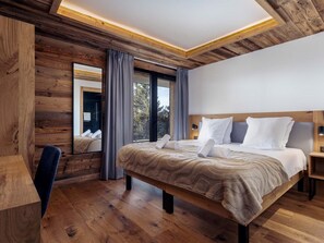 A modern hotel room with a wooden ceiling, a large bed with white linens, a desk, and a view of the outdoors. - Résidence l'Orée du Bois by Interhome (La Rosière)
