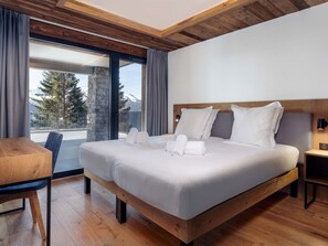 Ein modernes Hotelzimmer mit einem großen Bett, einem hölzernen Kopfteil, einem kleinen Tisch und Blick ins Freie.