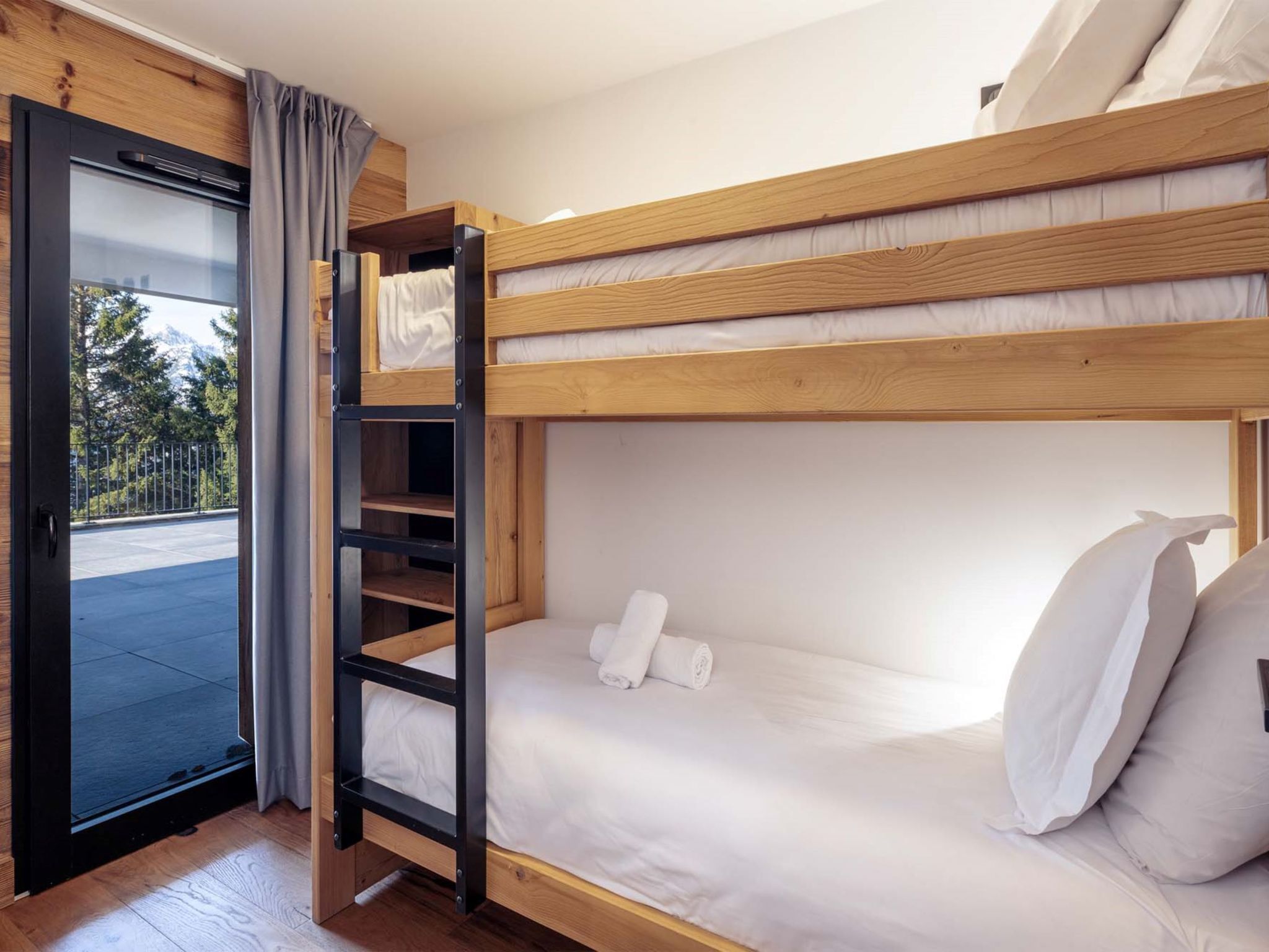 A bunk bed room with a wooden ladder, a door leading outside, and a view of the outdoors.