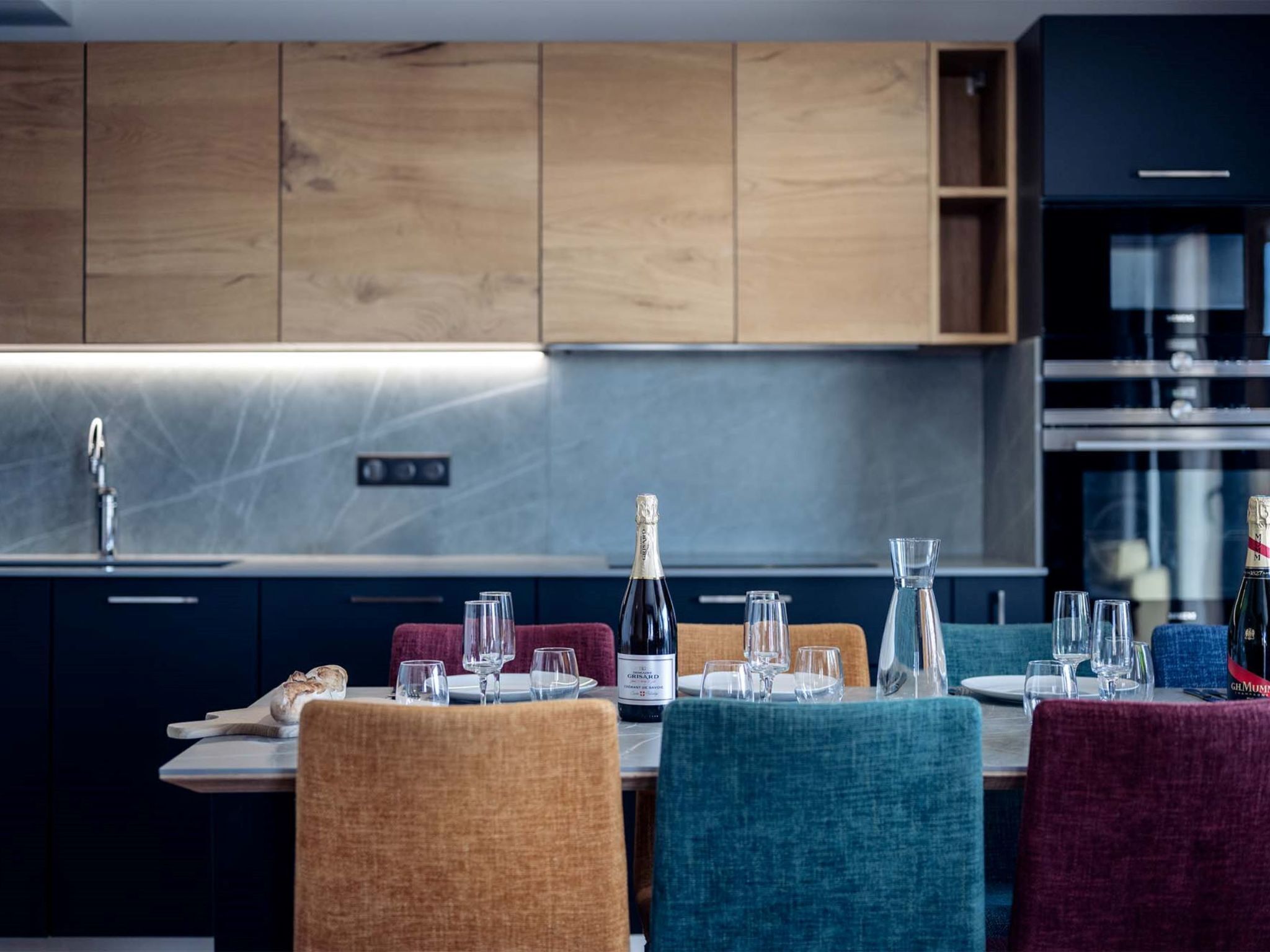 Une cuisine moderne avec des meubles en bois, un évier en acier inoxydable et un coin repas avec une table dressée pour deux personnes.