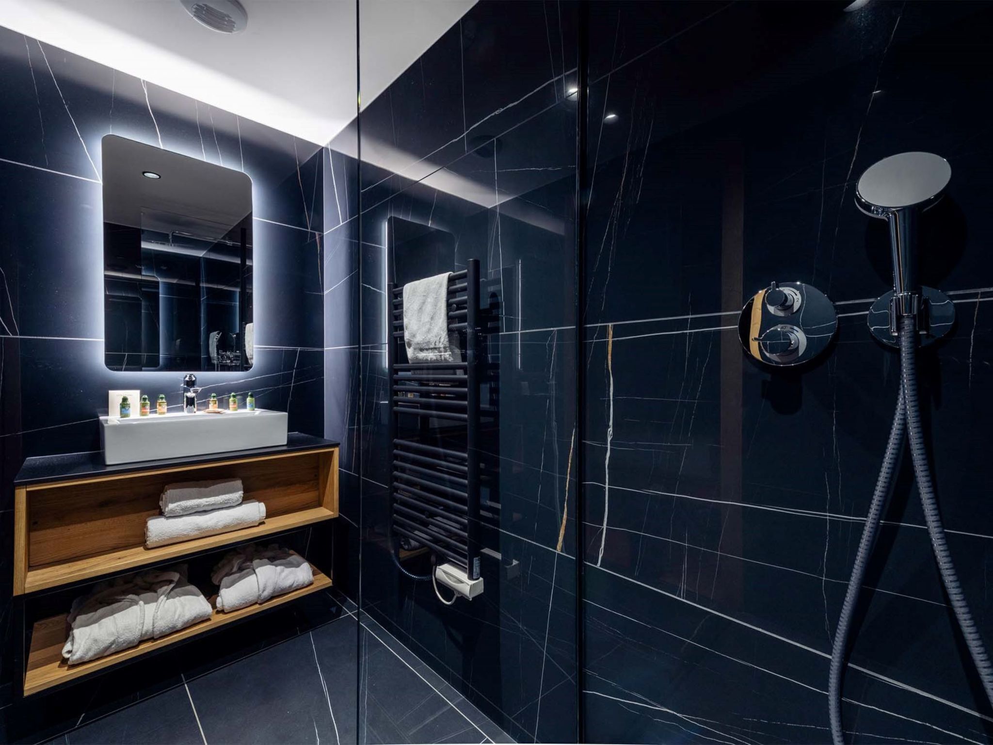 Une salle de bain moderne avec un lavabo en marbre noir, un miroir, un porte-serviettes et une douche équipée d’un pommeau de douche à main.