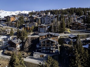 A mountainous resort with multiple buildings, including a prominent lodge with a large balcony and a ski lift in the background. - Résidence l'Orée du Bois by Interhome (La Rosière)