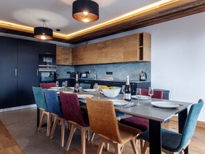 A modern kitchen with dark cabinets, wooden accents, and a dining area with colorful chairs and a table set for four.