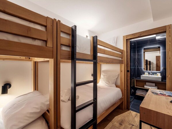 A bunk bed room with a wooden ladder, a desk, and a bathroom with a mirror and sink.