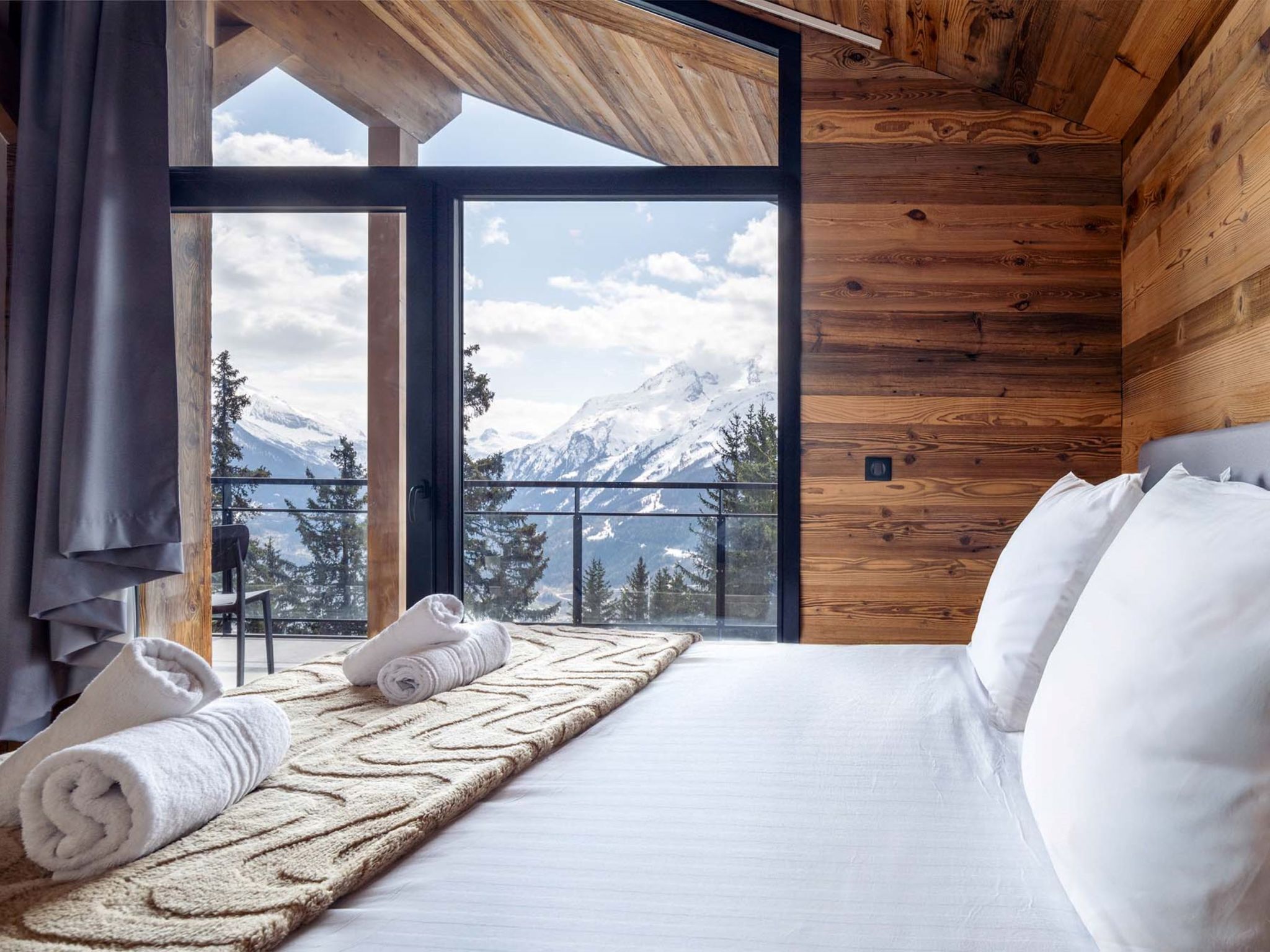 Ein Zimmer mit einem Bett, Blick auf Berge und einer Holzbalkendecke.