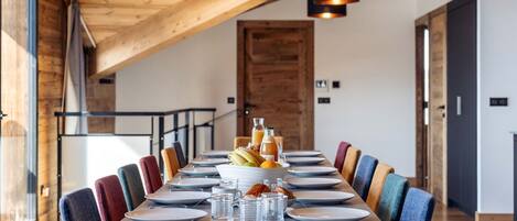 Un espace repas avec une longue table en bois, des chaises colorées et des luminaires suspendus.
