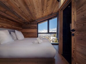 A wooden cabin bedroom with a bed, pillows, and a view of snow-capped mountains. - Résidence l'Orée du Bois by Interhome (La Rosière)