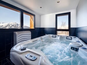 Ein modernes Badezimmer mit Whirlpool, großen Fenstern und Blick auf schneebedeckte Berge.